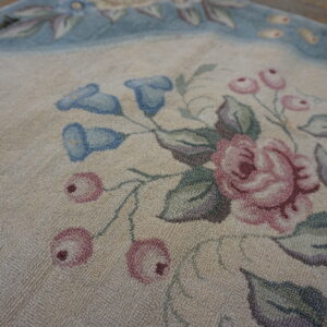 Detail of a looped floral rug featuring dusty rose, light blue, and green on a light background.