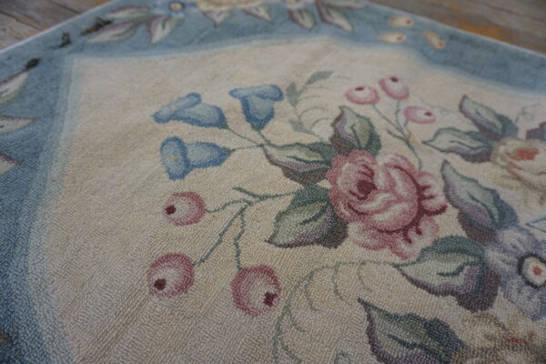 Detail of a looped floral rug featuring dusty rose, light blue, and green on a light background.
