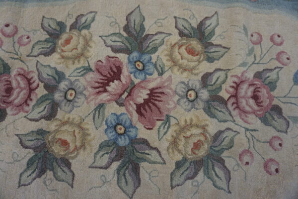 Muted floral rug with a cream background, dusty rose, blue, and pale yellow flowers, and looped texture.