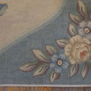 Muted low-pile floral rug shows cream, blue, and mauve flowers on a segmented background over wood flooring.