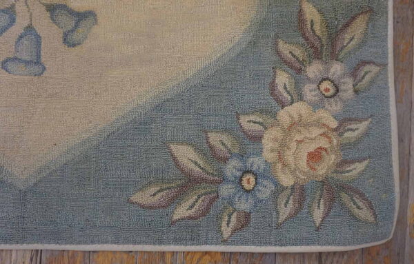 Muted low-pile floral rug shows cream, blue, and mauve flowers on a segmented background over wood flooring.