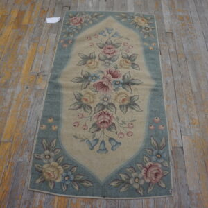 Beige and blue low-pile rug with a detailed floral pattern resting on distressed wood floorboards.