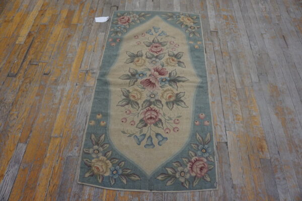 Beige and blue low-pile rug with a detailed floral pattern resting on distressed wood floorboards.