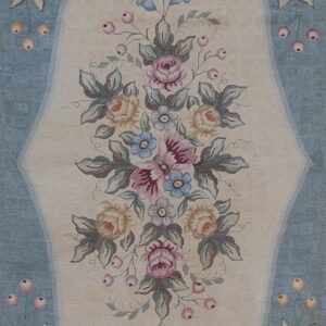 Low pile rug with an ornate pastel floral bouquet inside a cream medallion on a light blue ground.