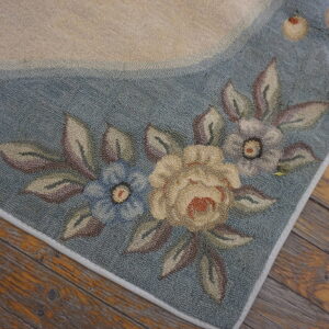 A textured rug border in dusty blue and cream displays a floral pattern on rustic wood floorboards.