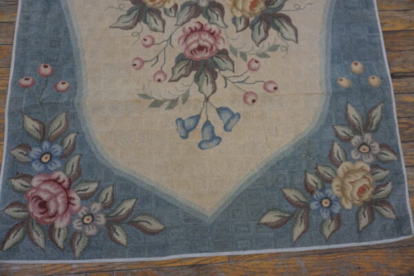 Floral rug with a beige field, blue border, pink and yellow roses, lying on exposed rustic wood floors.