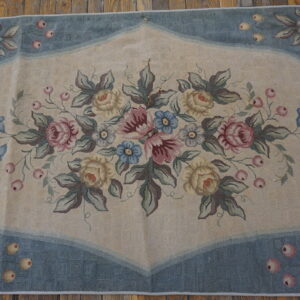 Low-pile rug with a beige field, blue border, and large central arrangement of pink and yellow roses.