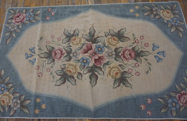 Low-pile rug with a beige field, blue border, and large central arrangement of pink and yellow roses.