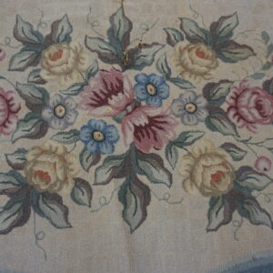 Textured rug close-up showing a dense floral bouquet pattern of pastel roses, blue flowers, and green leaves on a cream ground.