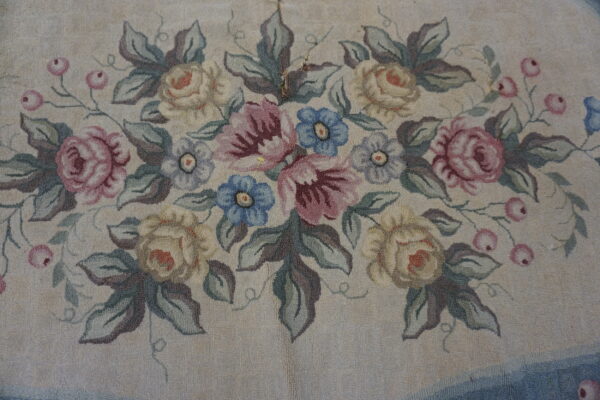 Textured rug close-up showing a dense floral bouquet pattern of pastel roses, blue flowers, and green leaves on a cream ground.