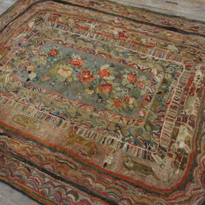 A textured rug with rounded corners, featuring a sage floral center and layered, earthy borders on wood.