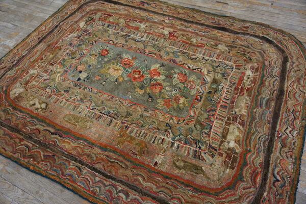 A textured rug with rounded corners, featuring a sage floral center and layered, earthy borders on wood.