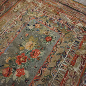 A textured gray rug with red and yellow florals is layered atop a multi-hued geometric border rug on wood flooring.