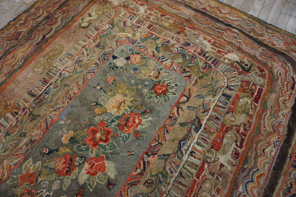 A textured gray rug with red and yellow florals is layered atop a multi-hued geometric border rug on wood flooring.