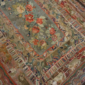 Highly textured, multicolored rug featuring a central floral field surrounded by complex, detailed borders.