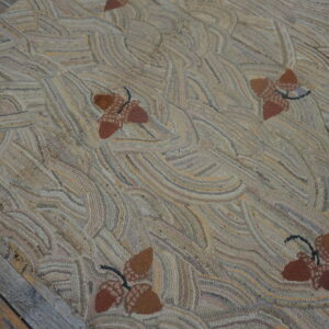 Highly textured hooked rug with brown acorn motifs and a swirling tan, beige, and gray background on wood planks.