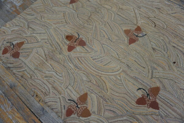 Highly textured hooked rug with brown acorn motifs and a swirling tan, beige, and gray background on wood planks.