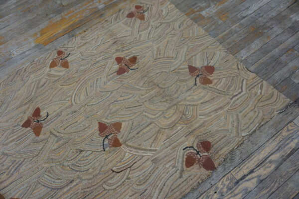 Textured beige rug with wavy lines and scattered brown acorn motifs rests on distressed gray wood planks.