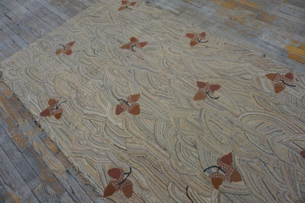 Highly textured tan rug featuring a repeating pattern of brown acorn clusters on gray distressed wood.