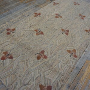 A beige hooked rug with an all-over wavy pattern and scattered brown acorn motifs rests on distressed gray wood floors.