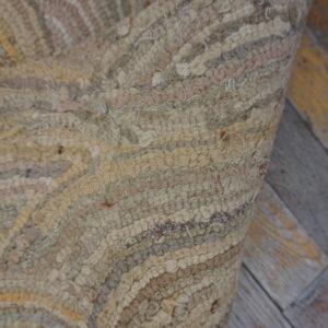 Close-up of a high-pile rug with wavy stripes in neutral beige, gray, and brown tones, lying on distressed wood floor.