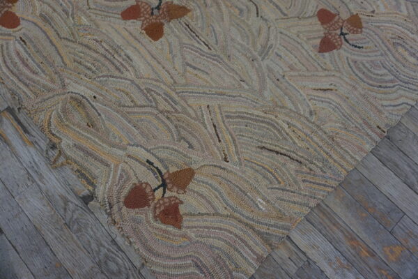 Rustic hooked rug in neutral tones with brown acorns resting on distressed grey wood planks.
