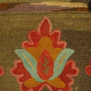 Detail of a moss green textured rug featuring a stylized red, orange, and teal floral design.