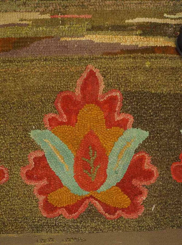Detail of a moss green textured rug featuring a stylized red, orange, and teal floral design.