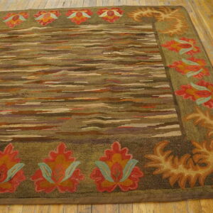 Textured rug featuring a striated center field and a thick olive border with stylized red and orange flowers on wood flooring.