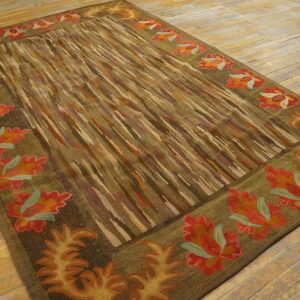 Earth-toned rug with red and orange floral borders and a striped center lies on light wood flooring.