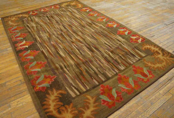 Earth-toned rug with red and orange floral borders and a striped center lies on light wood flooring.