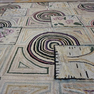 Textured rug with a tiled pattern of concentric spirals, abstract shapes, and floral designs in muted colors.