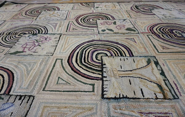 Textured rug with a tiled pattern of concentric spirals, abstract shapes, and floral designs in muted colors.