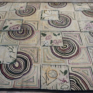 Textured low-pile rug with a cream patchwork design featuring abstract spirals and floral motifs in muted colors.