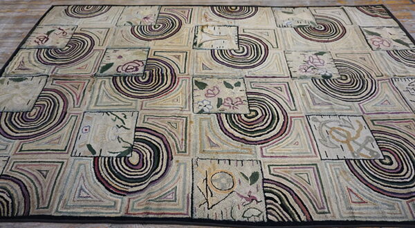 Textured low-pile rug with a cream patchwork design featuring abstract spirals and floral motifs in muted colors.