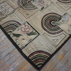 Low-pile rug with geometric blocks and floral patterns in cream, black, green, and purple on worn wood floors.