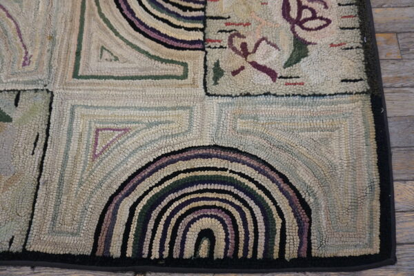 Muted multi-colored hooked rug detail showing geometric arches and floral shapes on wood planks.