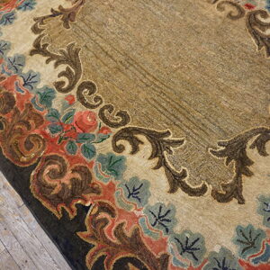 Tan rug featuring a dense floral and scrolled coral, blue, and brown border on distressed wood.