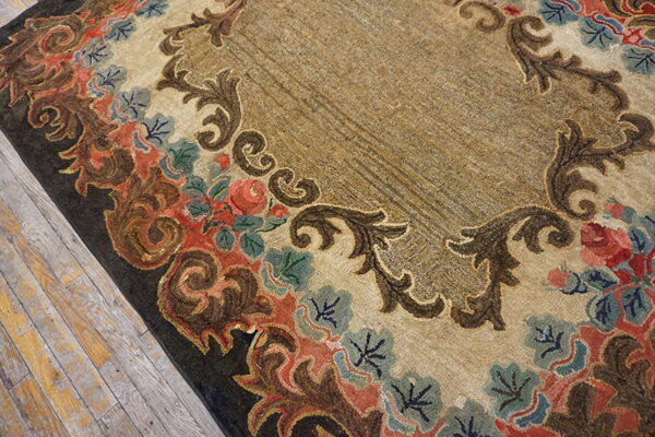Tan rug featuring a dense floral and scrolled coral, blue, and brown border on distressed wood.