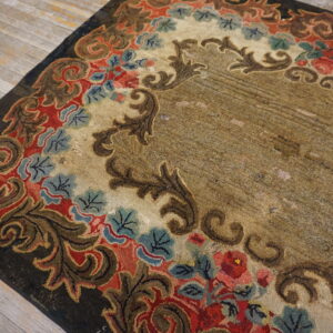Low-pile textured rug with red, blue, and brown floral scrollwork bordering a mottled tan center on distressed wood floors.