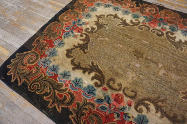 Low-pile textured rug with red, blue, and brown floral scrollwork bordering a mottled tan center on distressed wood floors.