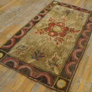 Rustic hooked rug with red floral motif and scalloped border on weathered wood flooring.