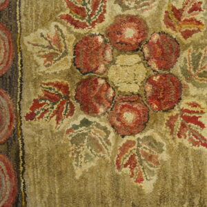 Khaki hooked rug with red floral medallion and striped border detail on light wood planks.