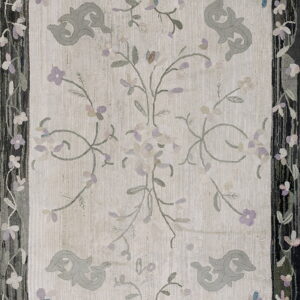 Pale rug with stylized gray motifs and purple floral vines, bordered by dark stripes and flowers.