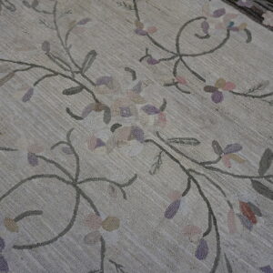 Textured beige rug with scrolling floral pattern in pastel pink, purple, and gray colors.