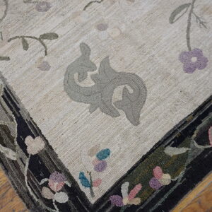 Close-up of a textured cream rug with gray stylized motifs and a dark, multi-colored floral border on wood flooring.