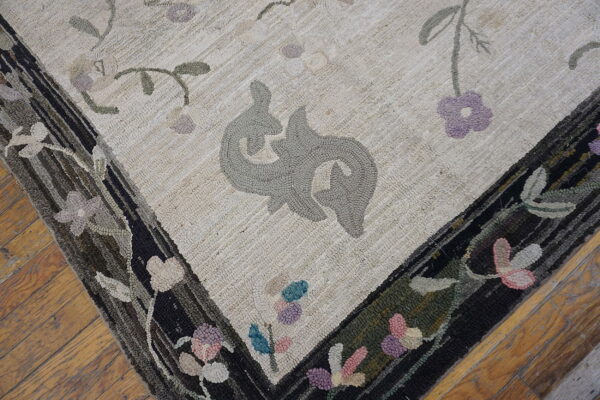 Close-up of a textured cream rug with gray stylized motifs and a dark, multi-colored floral border on wood flooring.