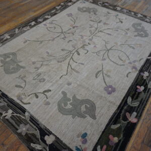 A cream hooked rug featuring sparse floral vines and gray scrolls, framed by a dark, floral border on wood floors.