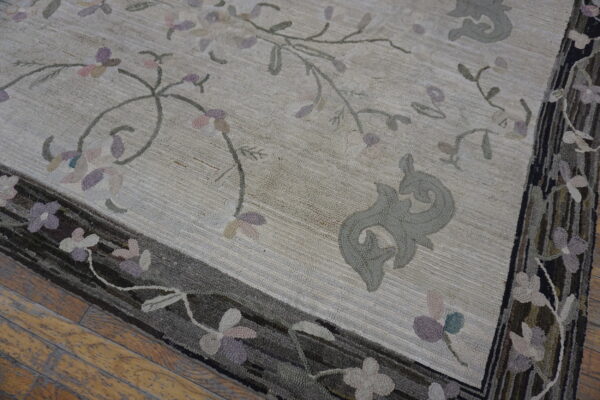 Textured cream rug with pale pink and lavender floral pattern and dark multi-toned border on wood.
