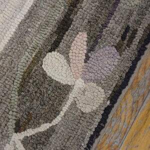 Textured hooked rug detail featuring gray, cream, pink, and purple floral motifs on distressed wood flooring.